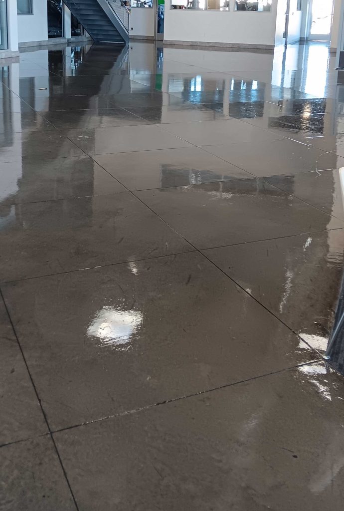 A large concrete floor covered with a thin layer of water, reflecting light and creating a glossy surface.
